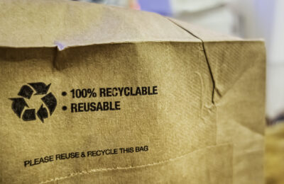 Brown paper bag that is 100% recyclable and reusable on a counter. A printed plea for user to recycle and reuse this bag as a form of packaging.
