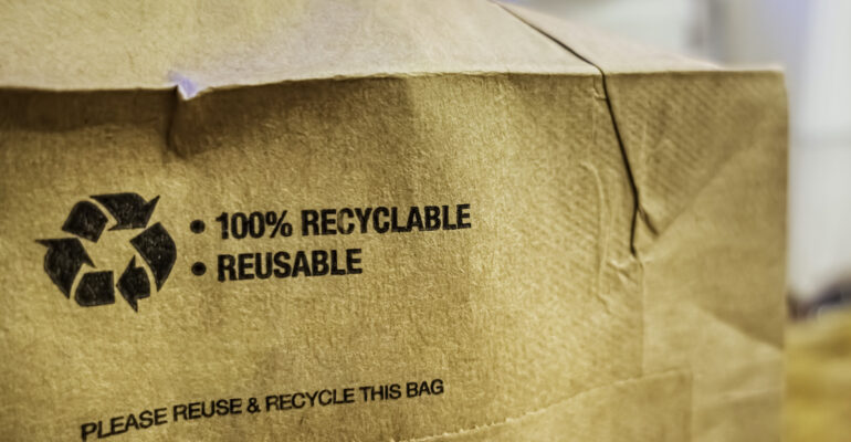 Brown paper bag that is 100% recyclable and reusable on a counter. A printed plea for user to recycle and reuse this bag as a form of packaging.