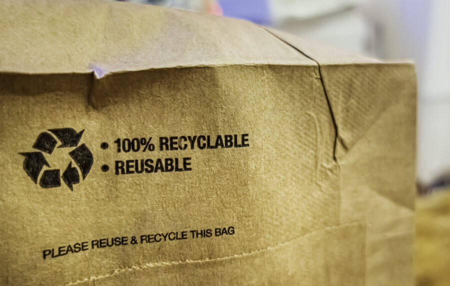 Brown paper bag that is 100% recyclable and reusable on a counter. A printed plea for user to recycle and reuse this bag as a form of packaging.