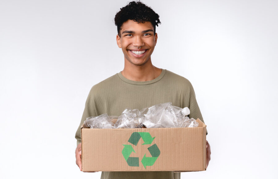 Adorable young african man holding a box with plastic bottles for recycling isolated over white background